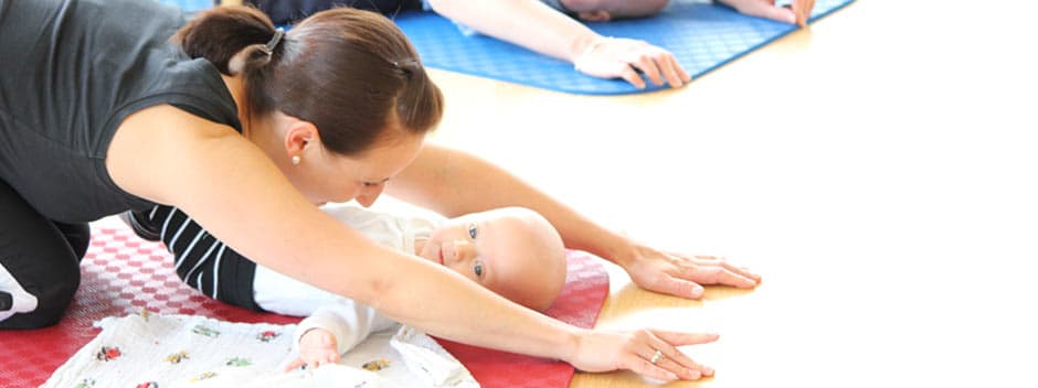 Mutter und Baby beim Yoga auf Matten